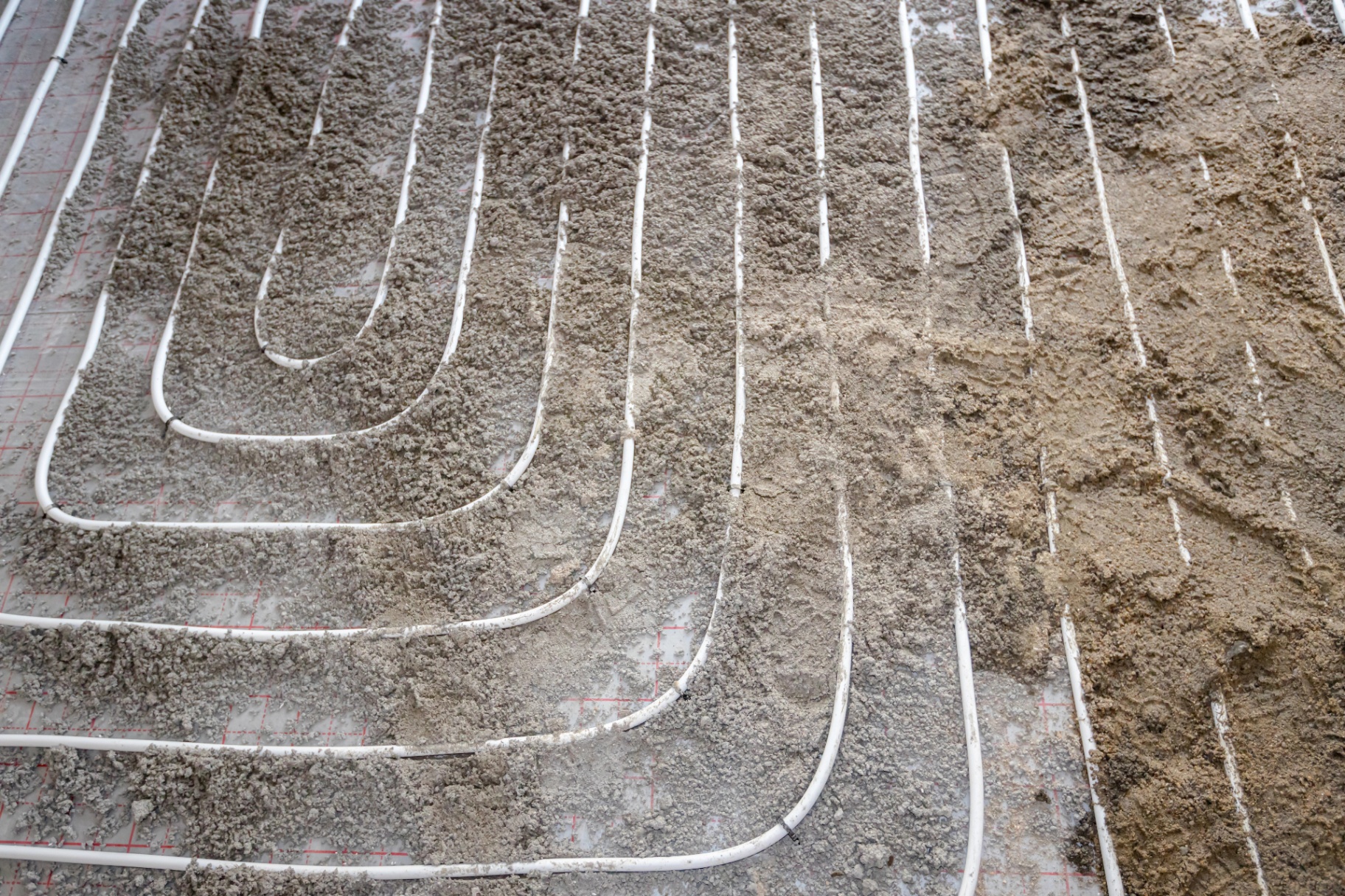 Zandcement wordt over vloerverwarmingsbuizen aangebracht als robuuste dekvloer
