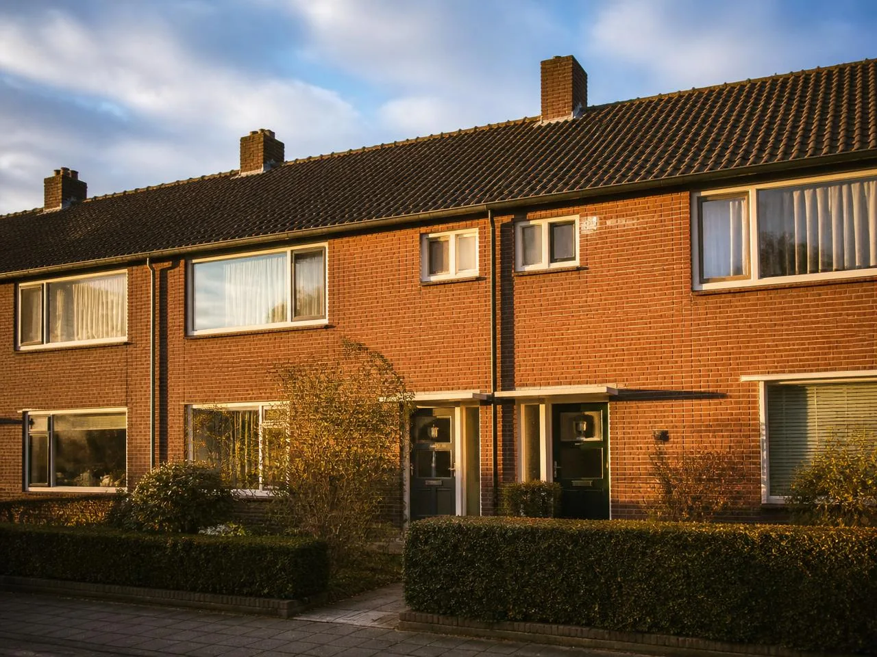 Typische Nederlandse jaren '70 rijtjeswoning van buiten — bakstenen gevel in warm namiddag-licht